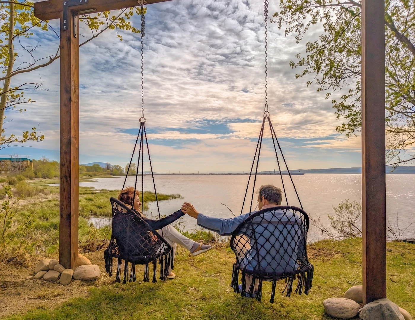 Un couple se tient la main dans les chaises suspendues face au Saint-Laurent, à Fleuve et Montagnes