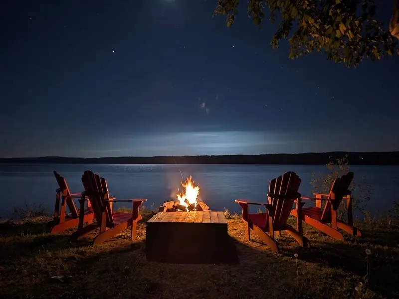 Feu et chaises Adirondack rouges au bord du fleuve, la nuit